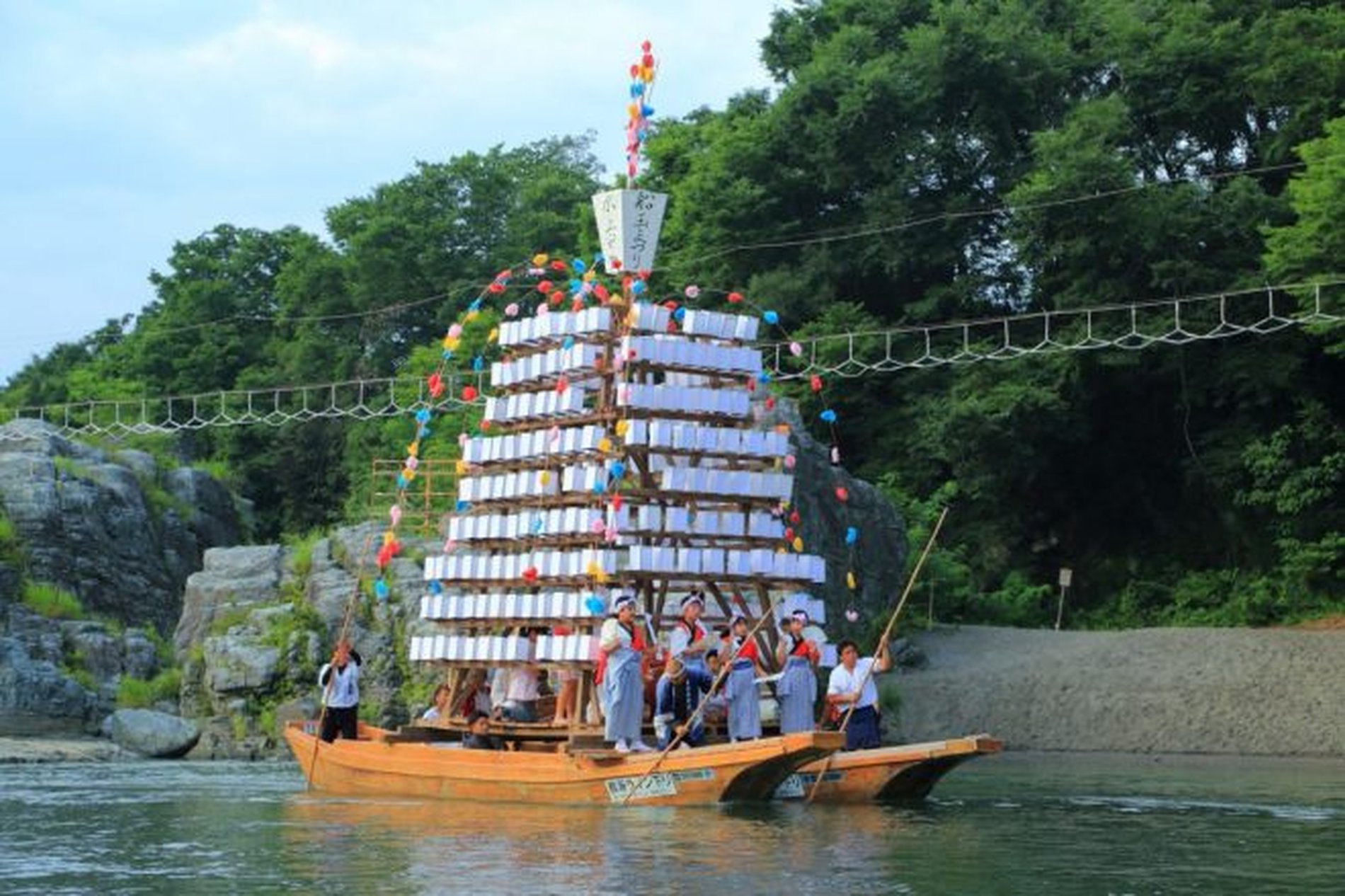 長瀞船玉まつりで、提灯を積んだ灯籠船を漕ぐ人々と、夏空の下を進む船の様子