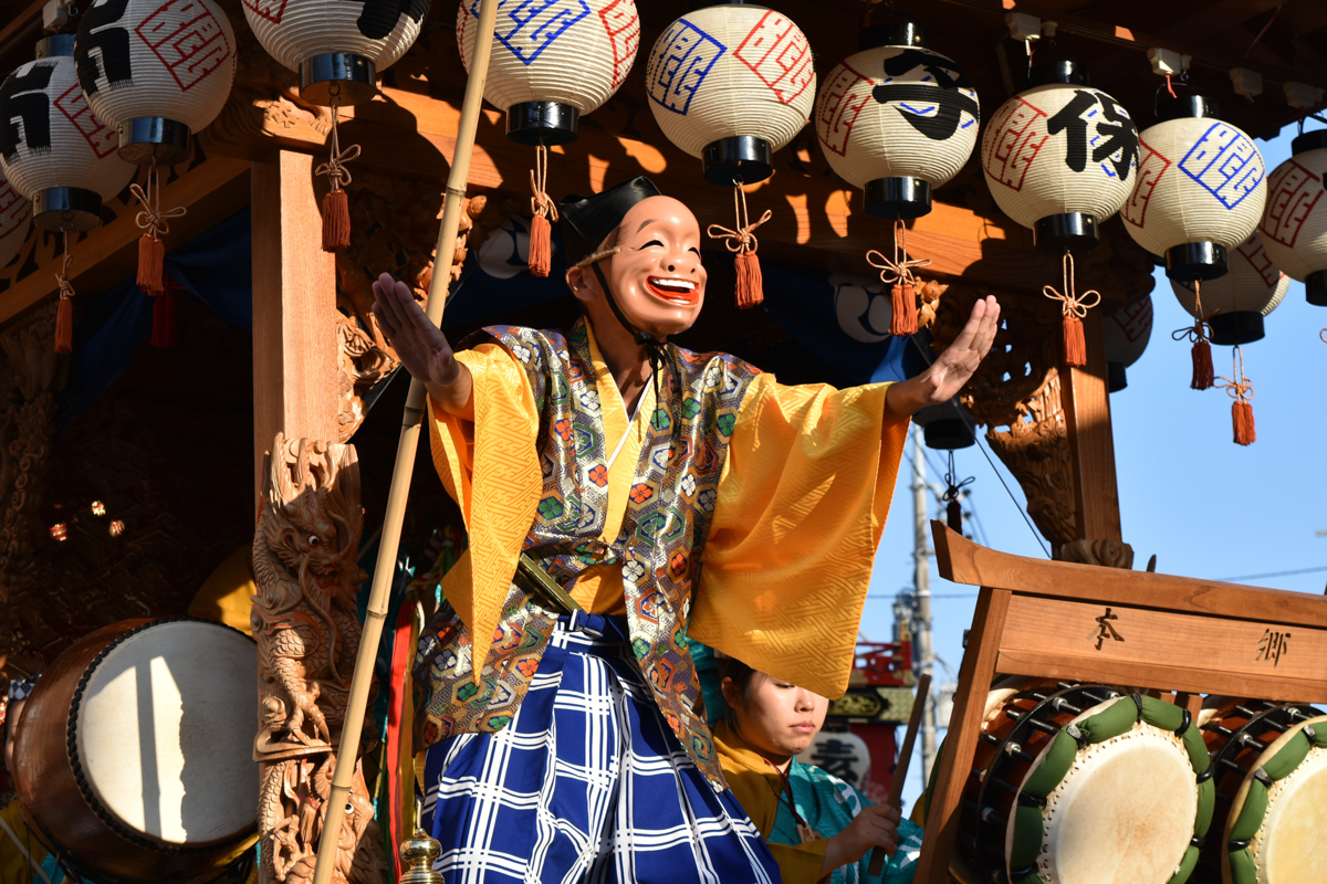 おかめ面の演者が山車上で舞を披露する飯能まつりの情景