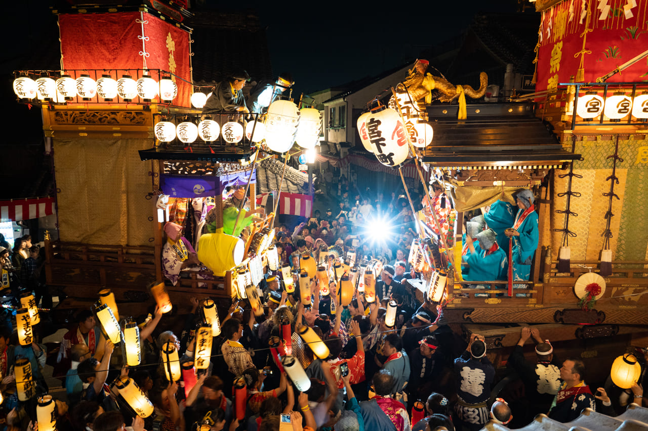 夜の川越まつりで、提灯を掲げた人々と向かい合う山車の様子