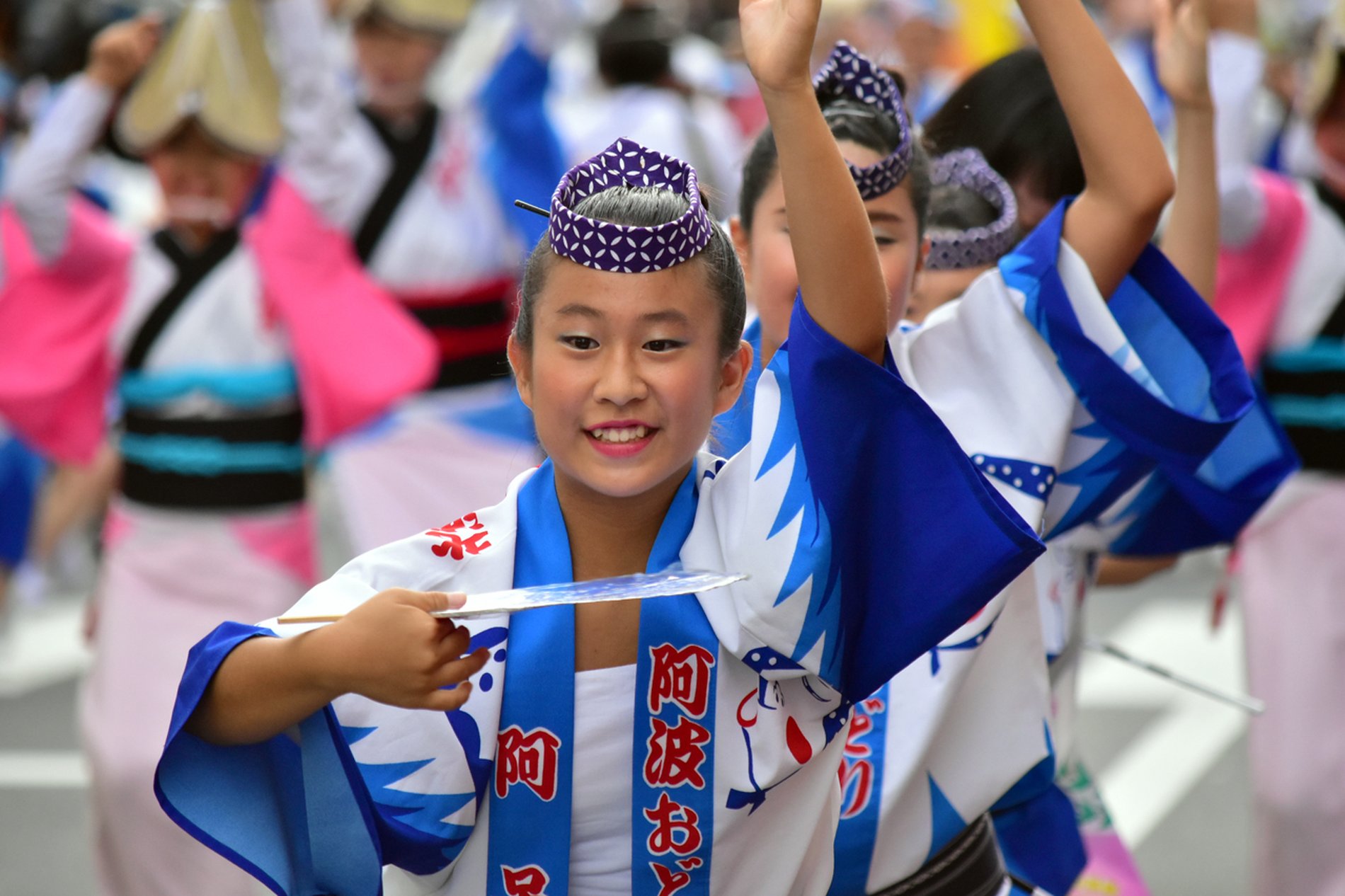 南越谷阿波踊りで、青と白の衣装を着た少女が笑顔で手を挙げて踊る様子