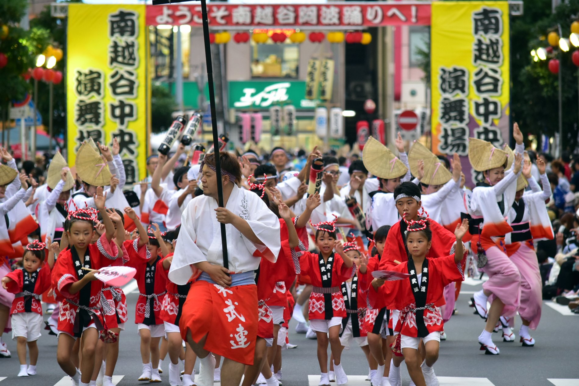 南越谷阿波踊りのパレードで、赤い衣装の子ども連と大勢の踊り手たちが街中を踊りながら進む様子