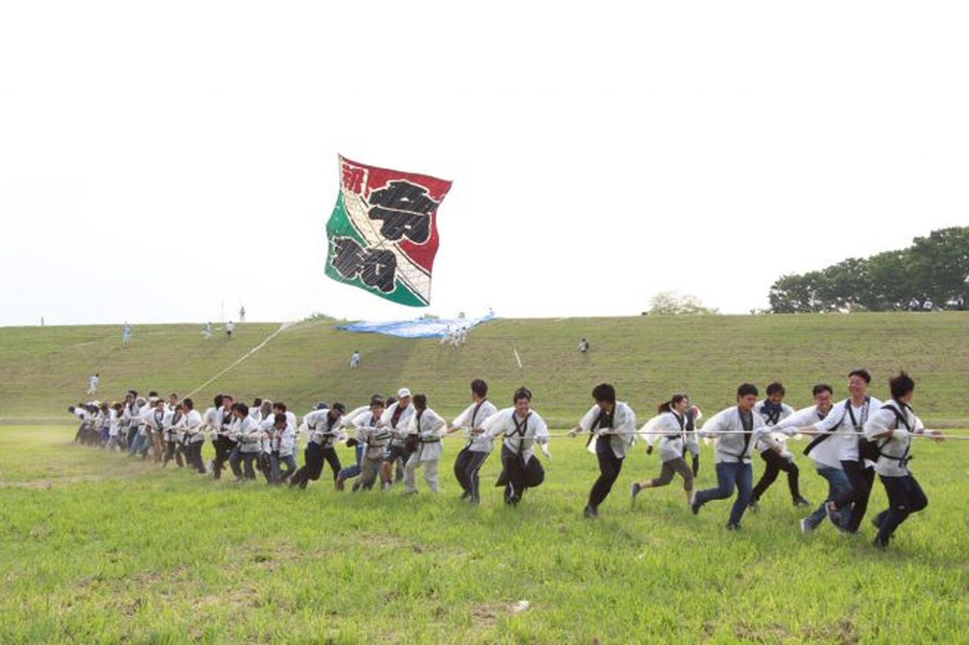 大きな凧を大人数で引きながら草原を駆ける参加者たち
