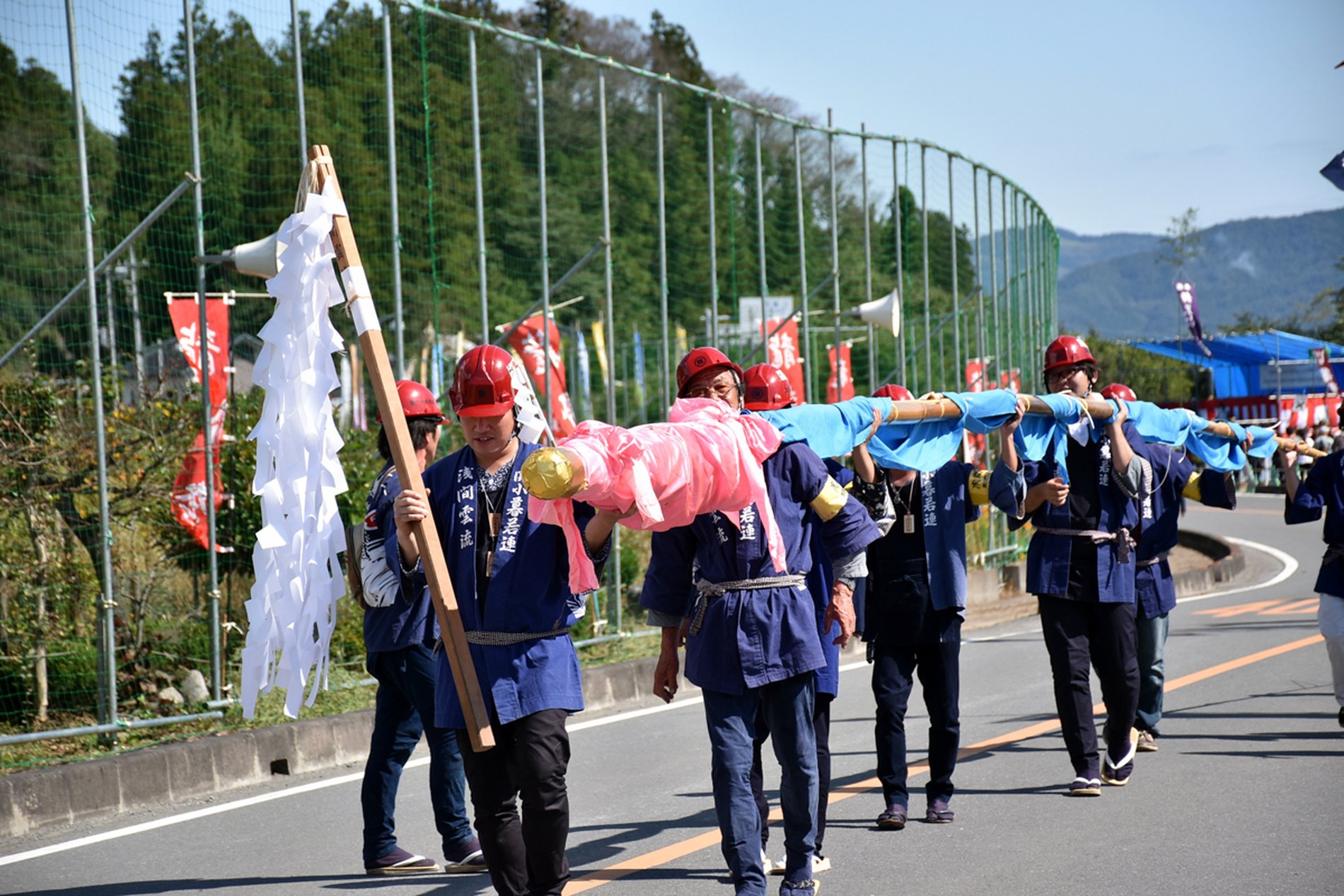 龍勢祭で法被とヘルメットを着けた担ぎ手たちが龍勢を担いで運ぶ行列